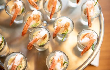 Small glasses filled with shrimp cocktail, garnished with herbs, arranged on a round metal tray.